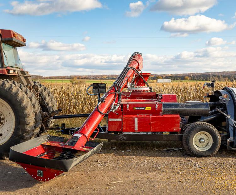 A Horning Mfg hammer mill hooked to a tractor in an autumn cornfield. 